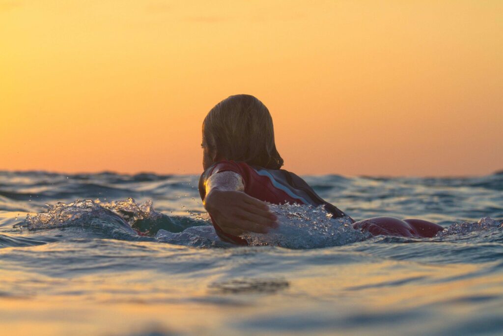 A surfer paddling out at sunset